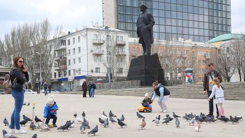 People with their children walk in a square in front of statue of Vladimir Lenin in the separatist-controlled Donetsk, eastern Ukraine.