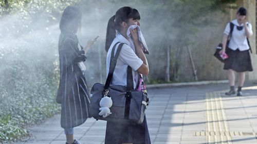 A high school student and other stand at a mist spray point for cooling while the maximum temperature exceeds 40 degrees Celsius in Tajimi City, Gifu Prefecture. Picture: AAP