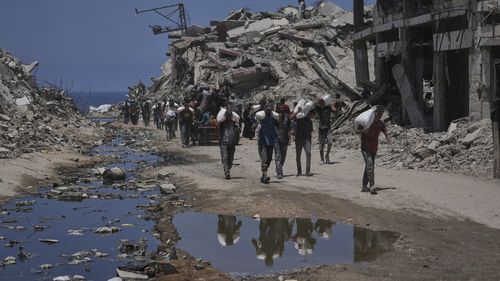 Palestinians carry sacks of flour unloaded from a humanitarian aid convoy that reached Gaza City from the northern Gaza Strip, Tuesday, July 22, 2025. (AP Photo/Jehad Alshrafi)