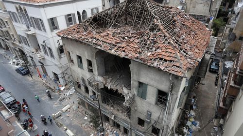 People pass in front of a house that was damaged during the last week's explosion that hit the seaport of Beirut, Lebanon, Tuesday, Aug. 11, 2020