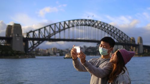 People wear face masks in front of the Sydney Harbour Bridge in Sydney, Monday, March 9, 2020.