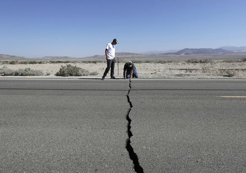 Ron Mikulaco and his nephew, Brad Fernandez, examine a crack caused by an earthquake on Highway 178, July 6, 2019, outside of Ridgecrest, California.