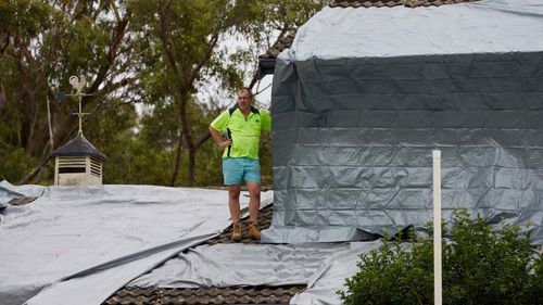 A resident is seen on the roof of a house that was damaged in a hail storm overnight in Berowra Heights.