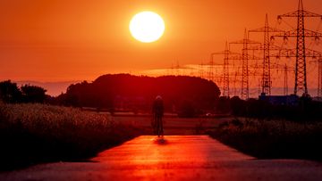 A man rides his bike on a small road with a sunset in the distance