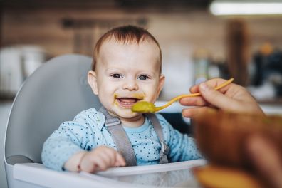 Portrait of smiling baby boy at home being fed by his dad.