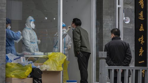 BEIJING, CHINA - MARCH 25: A health worker wears a protective suit as she performs a nucleic acid test to detect COVID-19 on a local resident at a pop-up testing site in the street on March 25, 2022 in Beijing, China. China has stepped up efforts to control a recent surge in coronavirus cases across the country, locking down the entire province of Jilin and the city of Shenyang and putting others like Shenzhen and Shanghai under restrictions. Local authorities across the country are mass testing