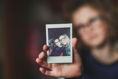 Little girl who's face is out of focus reaches out and shows an instant film photo of her and her mother to the camera.