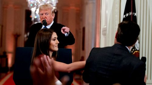 President Donald Trump watches as a White House aide reaches to take away a microphone from CNN journalist Jim Acosta during a news conference in the East Room of the White House in Washington.