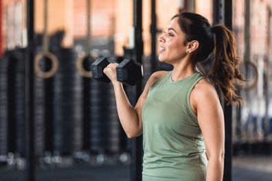 A profile view of a powerful mid adult woman using weights as part of her workout at the fitness center.