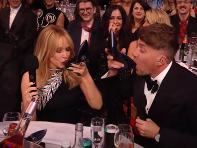 Kylie Minogue and Roman Kemp do a shoey during the 2024 Brit Awards