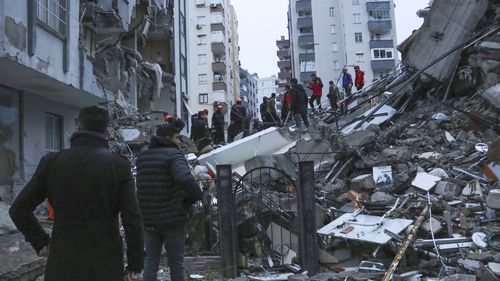 People and rescue teams try to reach trapped residents inside collapsed buildings in Adana, Turkey, Monday, Feb. 6, 2023 