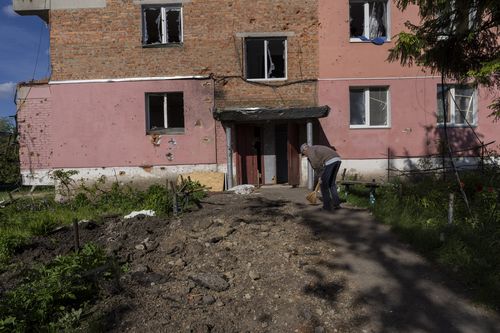 Resident Alexander, 67, sweeps the entrance of his building damaged by shelling in Kutuzivka, near Kharkiv, eastern Ukraine, Friday, May 27, 2022. (AP Photo/Bernat Armangue)