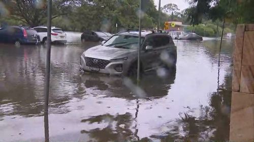 A car is trying to get through floodwaters, which have almost reached the top of its tiers in Manly Vale. 