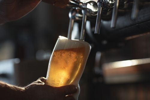 Fresh beer filling the glass directly from the tap.  With extra foam spilling over glass.