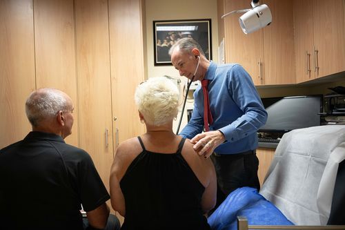 Um clínico geral durante uma consulta com dois pacientes.
