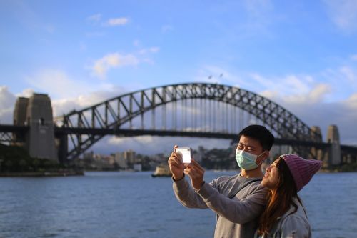 People wear face masks in front of the Sydney Harbour Bridge in Sydney, Monday, March 9, 2020.