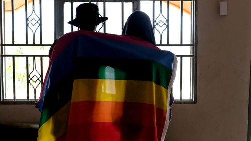 A gay Ugandan couple cover themselves with a pride flag