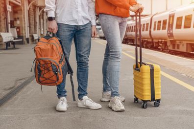 Travelers with a backpack and yellow suitcase waiting for a train at the train station. The couple missed the train. Travel concept.