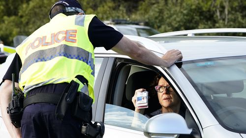 A motorist shows identifcation at a checkpoint on the Gold Coast Highway at Coolangatta on the Queensland/NSW  border , Thursday, March 26, 2020.