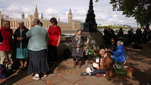 Well-wishers reading books, sitting on fold out chairs and chatting by the river Thames across from the houses of Parliament ahead of the procession for the Lying-in State of Queen Elizabeth II on September 14, 2022 in London, England.  Queen Elizabeth II's coffin is taken in procession on a Gun Carriage of The King's Troop Royal Horse Artillery from Buckingham Palace to Westminster Hall where she will lay in state until the early morning of her funeral.  Queen Eliz