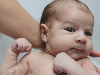 Closeup of newborn girl in the bathtub held by her mother