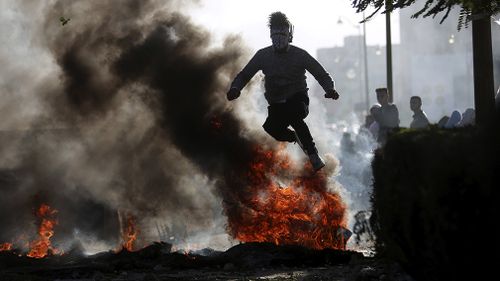 A protester jumps over burning tiers in Ramallah. (AAP)