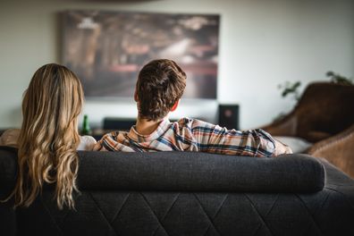 Rear view of a couple relaxing on sofa in the living room and watching a movie on TV