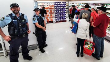 Police Officers watch as people queue for a delivery of toilet paper, paper towel and pasta at Coles Supermarket, in Sydney during March, 2020.