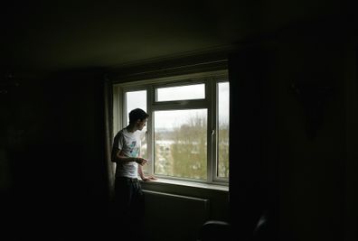 Man depressed standing at window at home.