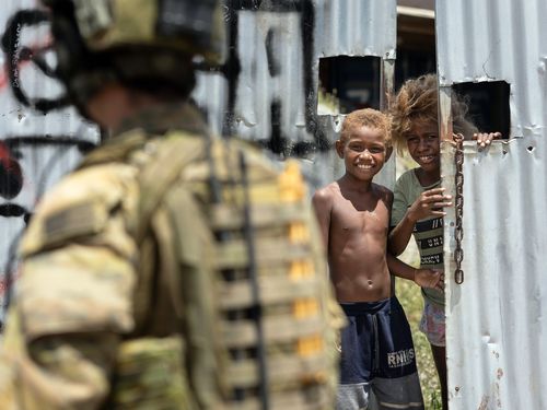 An Australian Army Corporal is greeted by a local child in Honiara, Solomon Islands