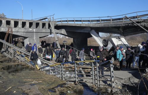 Ucrainenii traversează o cale improvizată pe sub un pod distrus în timp ce fug din Irpin, la aproximativ 25 km (16 mile) nord-vest de Kiev, vineri, 11 martie 2022. Suburbiile de nord-vest a Kievului, cum ar fi Irpin și Bucha, au suportat focurile și bombardamentele rusești de peste o săptămână. determinând locuitorii să-și părăsească locuința.  (AP Photo/Efrem Lukatsky)