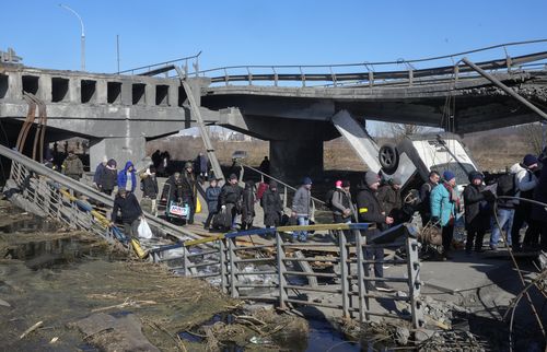 Ucrainenii traversează o cale improvizată pe sub un pod distrus în timp ce fug din Irpin, la aproximativ 25 km (16 mile) nord-vest de Kiev, vineri, 11 martie 2022. Suburbiile de nord-vest a Kievului, cum ar fi Irpin și Bucha, au suportat focurile și bombardamentele rusești de peste o săptămână. determinând locuitorii să-și părăsească locuința.  (AP Photo/Efrem Lukatsky)