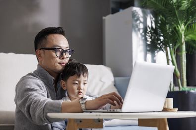 Asian middle-aged men work with notebooks at home. The son sat and played in his arms. During the pandemic, people worked from home.