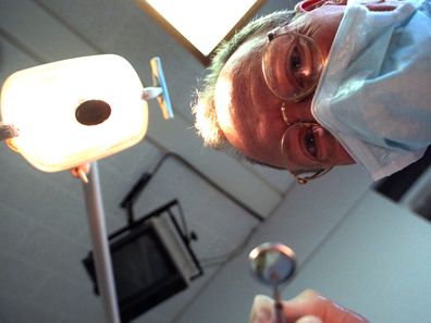A dentist in a mask leans over a patient while carrying out dental work.