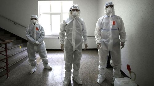 Health officials wearing protective gear prepare to spray disinfectant to help reduce the spread the new coronavirus ahead of school reopening in a cafeteria at a high school in Seoul, South Korea