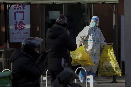 Un lucrător medical îmbrăcat în îmbrăcăminte de protecție poartă saci galbeni cu deșeuri medicale de la o clinică de febră din Beijing, luni, 19 decembrie 2022. 