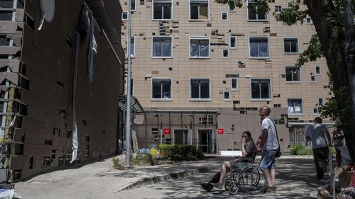 A man hauls a wheelchair with a girl in front of Okhmatdyt children's hospital hit by Russian missiles