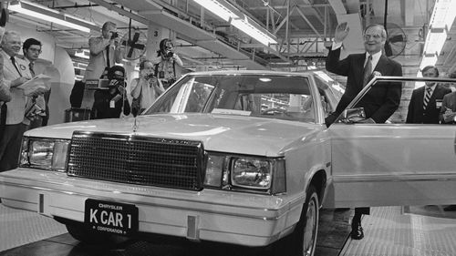 Lee Iacocca sits on the hood of K Car Number One, a Plymouth Reliant, in Detroit.