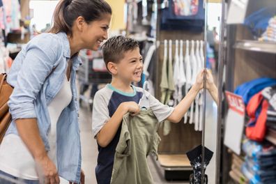 A mother lets her son pick out a new shirt while shopping after school.