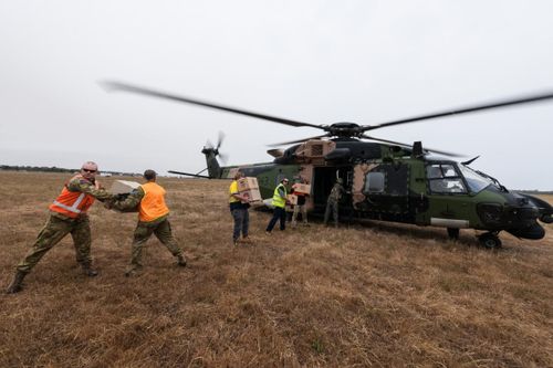 Soldiers and ground staff at at Bairnsdale Airport load a Navy MRH-90 helicopter with food and water to be airlifted to Cann River in Gippsland, Victoria