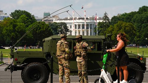 Os membros da região da Região Columbia National Guard conversam na frente da Casa Branca como um cavaleiro passando pela scooter.
