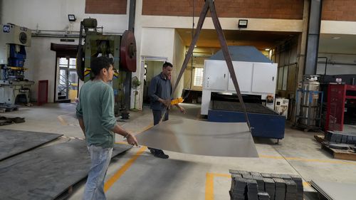 Workers move a large steel sheet to place in a laser cutting machine at a factory in a suburb of Bengaluru, India.