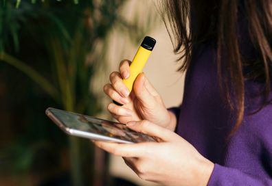 Yellow disposable electronic cigarette in a woman's hand. Modern online communication.