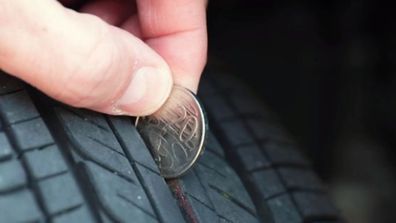 Man using 20 cent coin to check wear on tyre treads