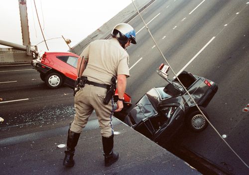 In this 1989 file photo, a California Highway Patrol officer checks the damage to cars that fell when the upper deck of the Bay Bridge collapsed onto the lower deck after the Loma Prieta earthquake in San Francisco. 