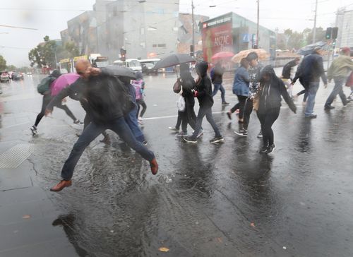 People are seen in Flinders Street, Melbourne, dashing from the rain. (AAP)