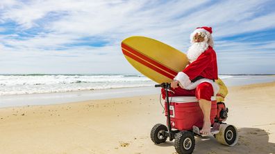 Santa Claus relaxing after Christmas riding a motorised esky cooler on the beach
