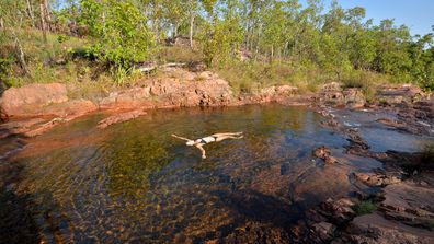 A woman in a black bikini floats on her back in the clear waters of a rock pool in Litchfield National Park in the Northern Territory Australia