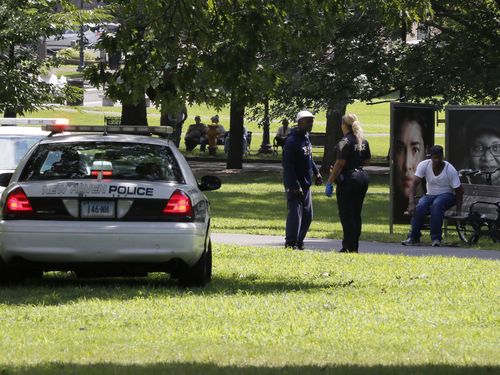 A police officer speaks to a man walking on New Haven Green, Wednesday, Aug. 15, 2018, in New Haven, Conn. A city official said more than a dozen people fell ill from suspected drug overdoses on the green and were taken to local hospitals. 