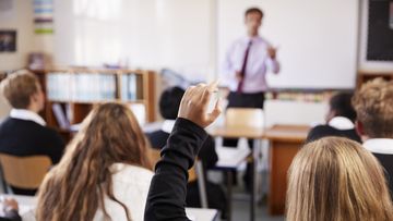 Female Student Raising Hand To Ask Question In Classroom